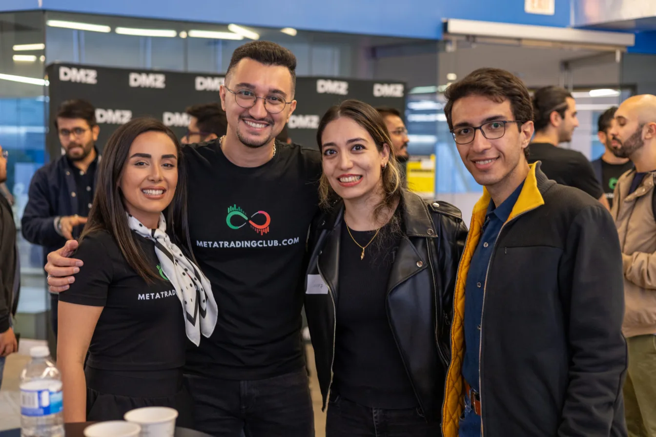 Four Meta Trading Club members in club shirts at a networking event