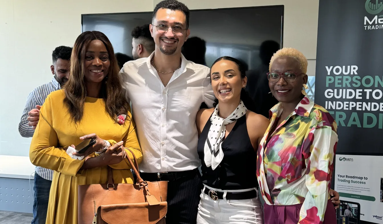 Four Meta Trading Club members at a meetup, standing beside a club banner