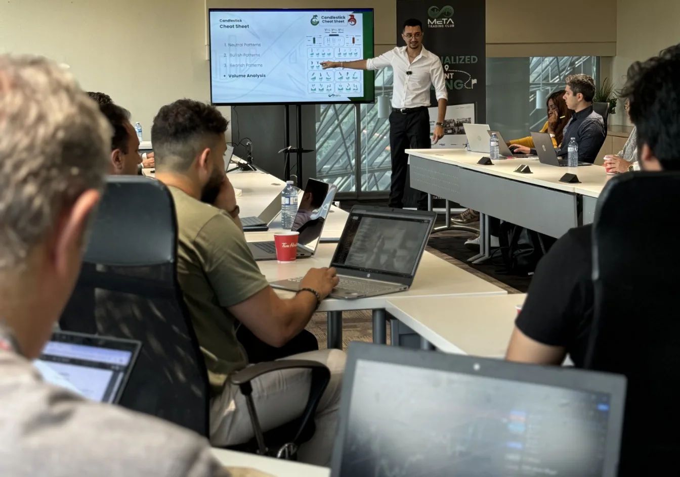 Attendees working on laptops while a presenter walks through charts at a Meta Trading Club workshop